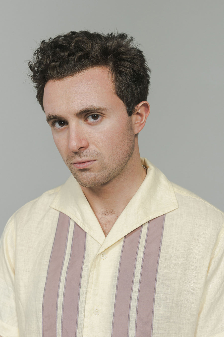 A strong portrait photo of a man in a white shirt with mauve stripes