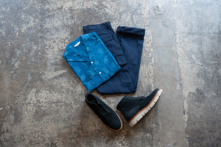 A top down shot of a folded button down, blue cargo pants and black boots.