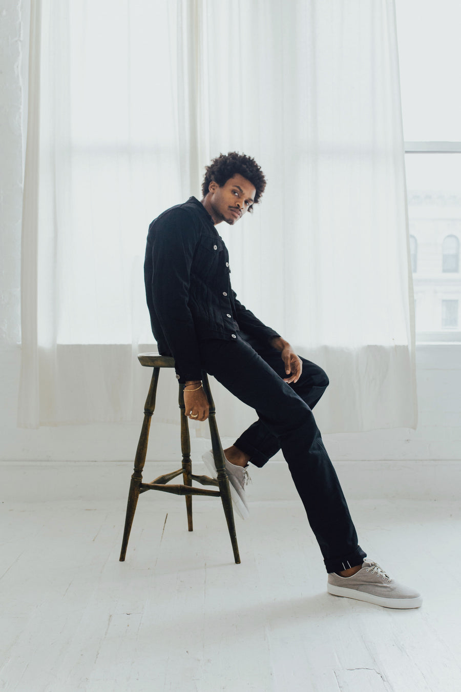 Model poses on a stool wearing 3sixteen jacket and jeans