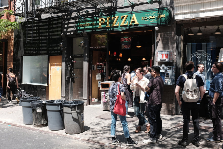 Exterior shot of Prince St. Pizza with customers waiting outside.