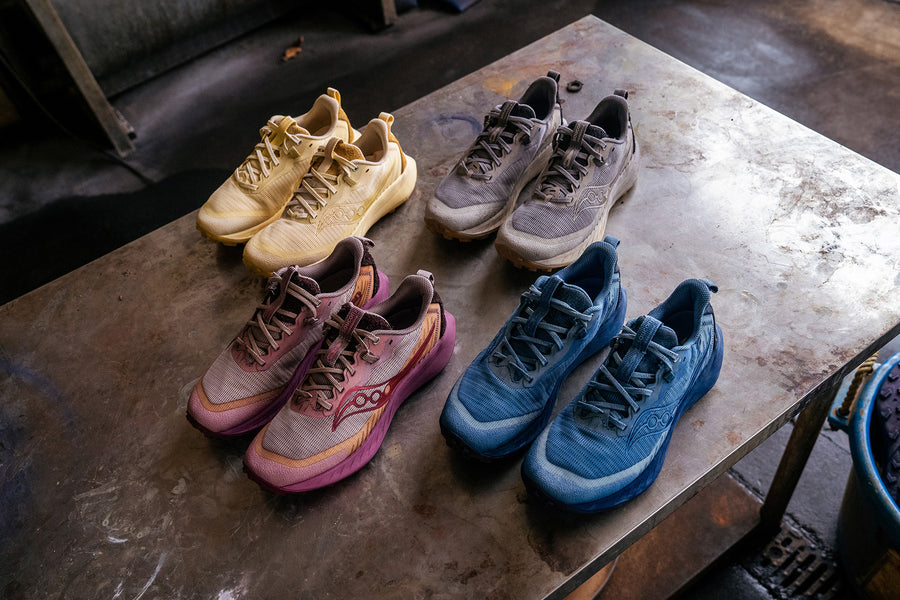 Four pairs of sneakers - dyed yellow, black, pink and blue - on a metal table.