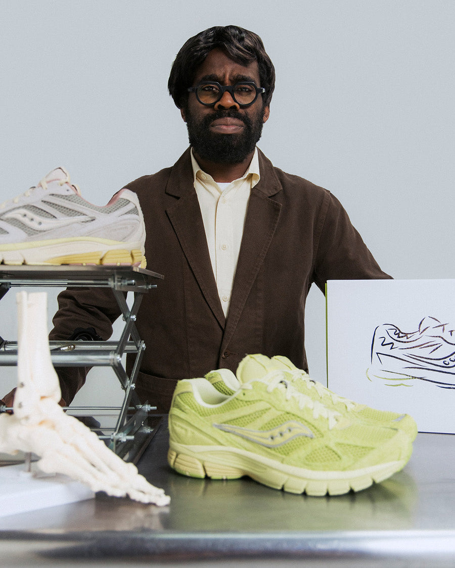 A man stands with two pairs of Saucony sneaker on a table.