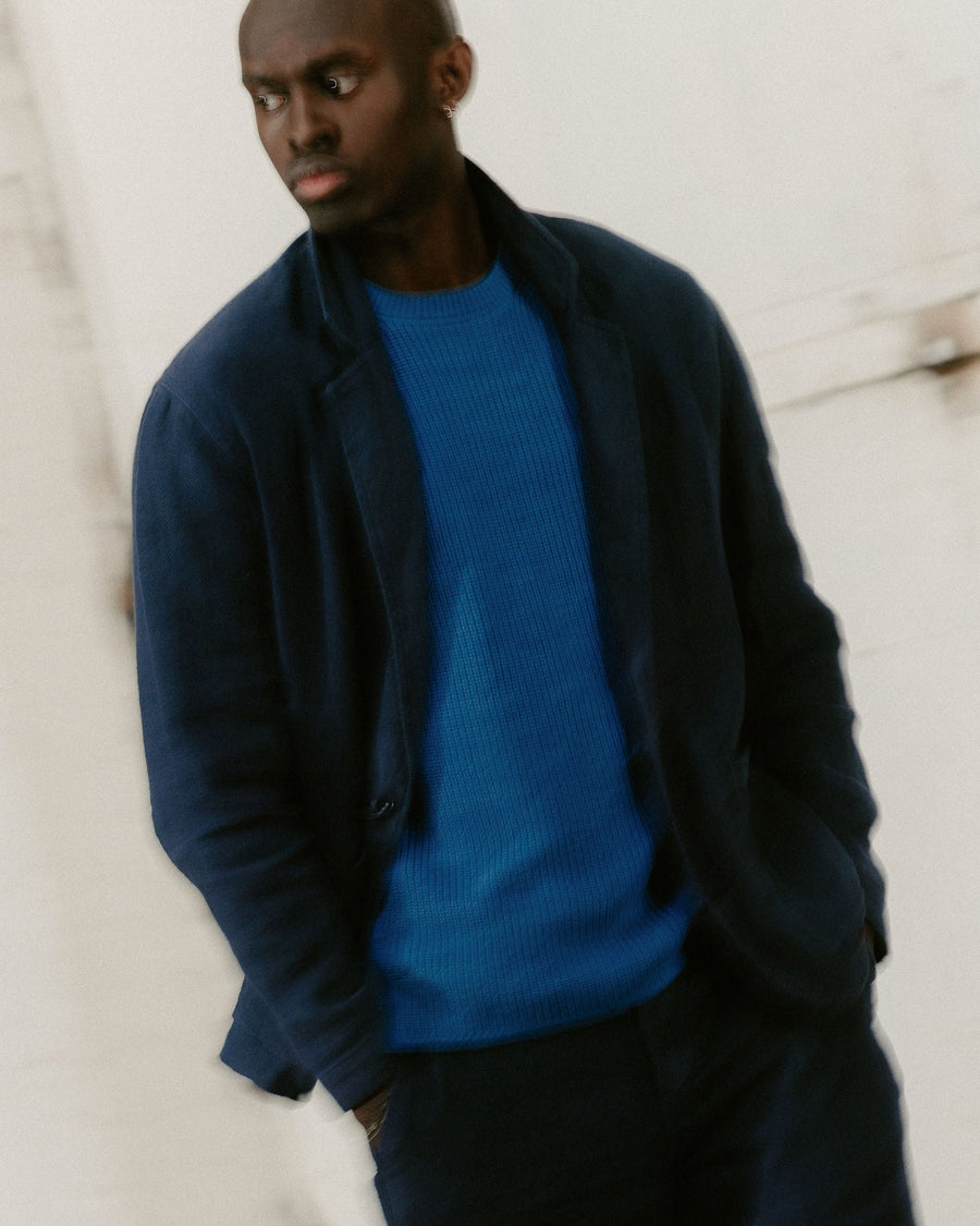 A blurry photo of a man in a navy blazer over a light blue sweater.