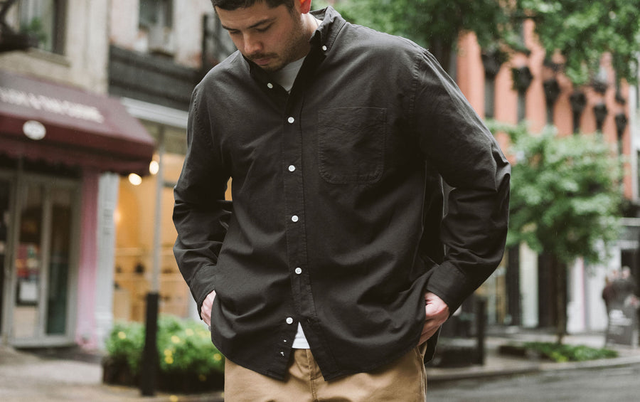 A man in a black oxford puts his hands into his pant pockets.