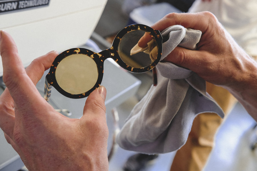 A man holds a finished pair of yellow round-lens sunglasses in his hands.
