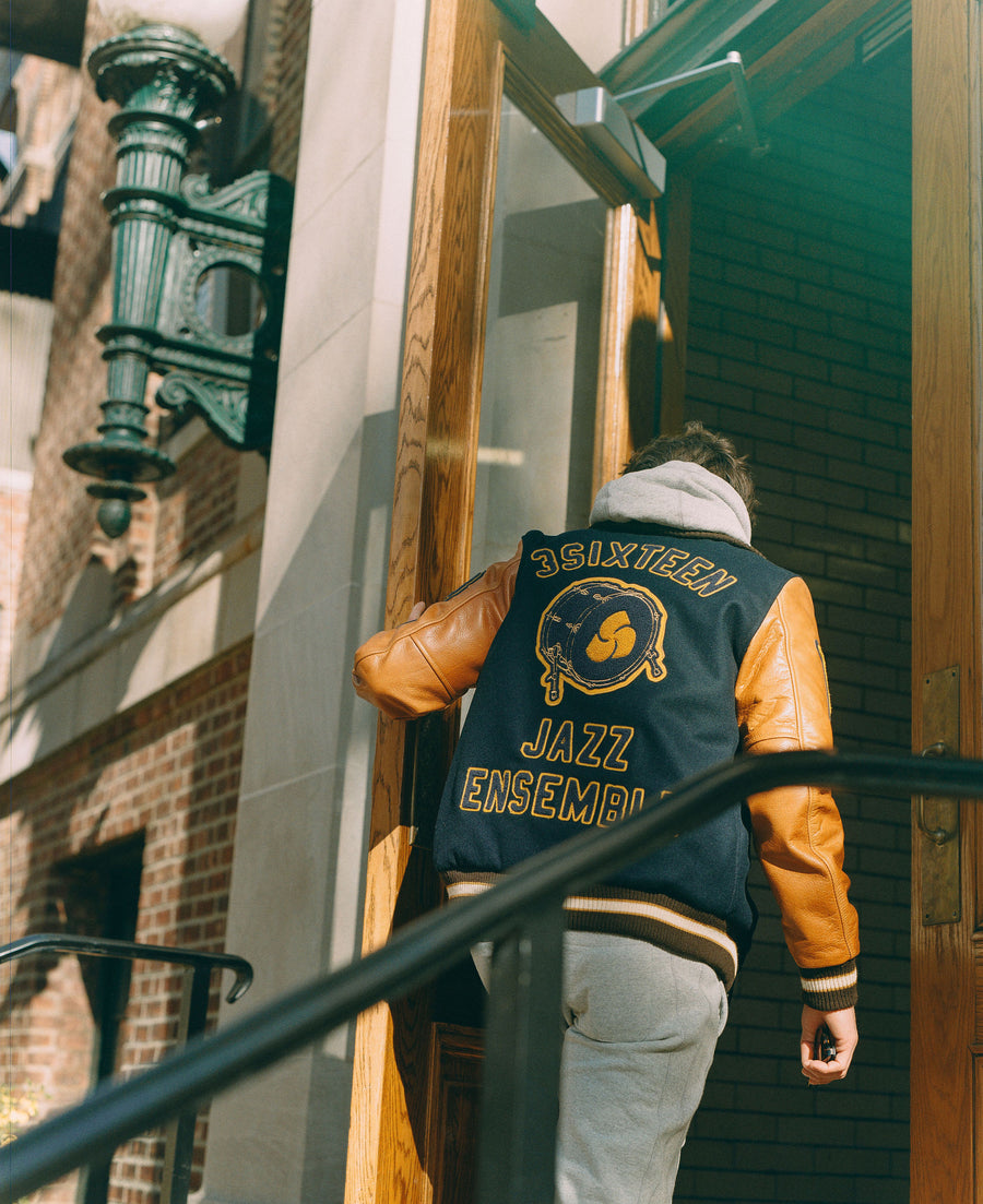 A man in a navy varsity jacket walks into a classroom door.
