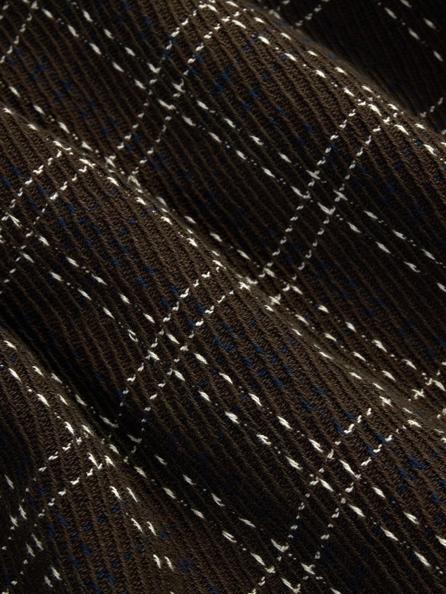 Close-up of a dark brown ribbed knit fabric with a subtle diamond windowpane pattern in white and blue.
