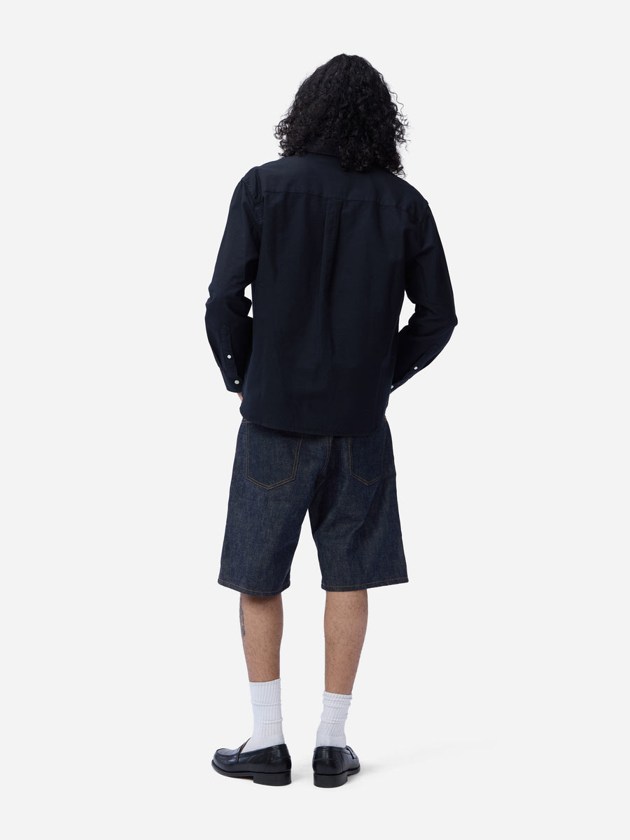 Person wearing a black long-sleeve shirt and denim shorts on a white background