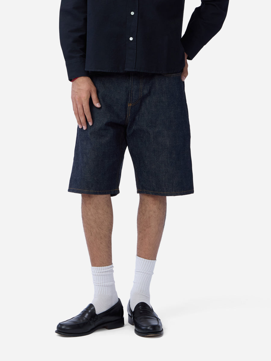 Person wearing dark denim shorts, black shoes, and white socks on a white background