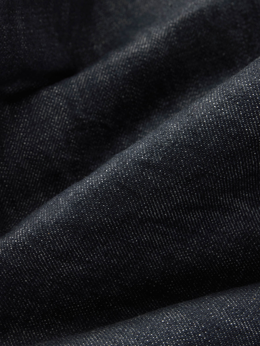 A close-up of dark charcoal gray denim fabric with a fine twill texture and soft folds.