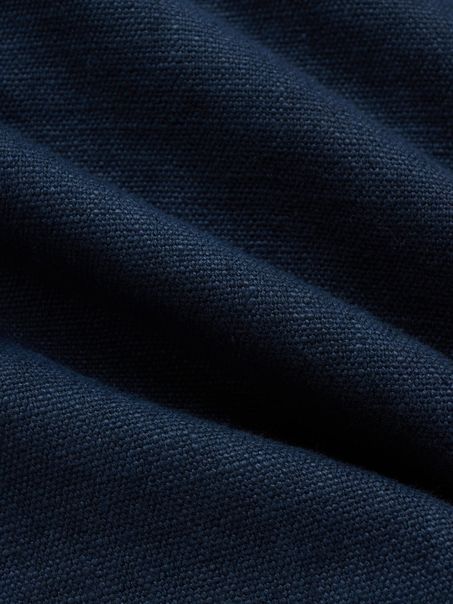 A close-up of dark navy blue fabric with a fine woven texture, shown with soft folds and shadows.