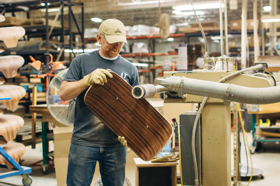 A man sands down the edges of a plywood shell.