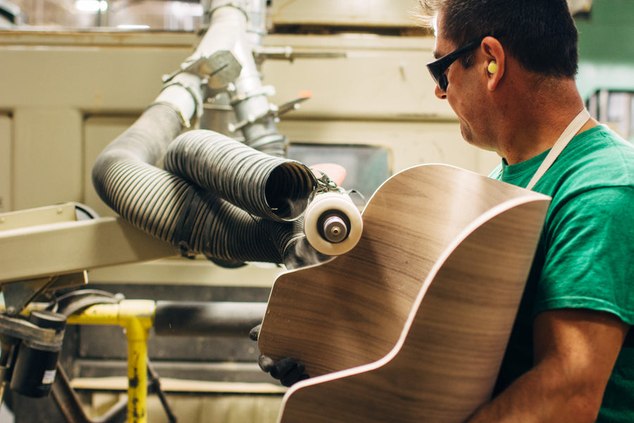 A man polishes the edges of a bent plywood shell.