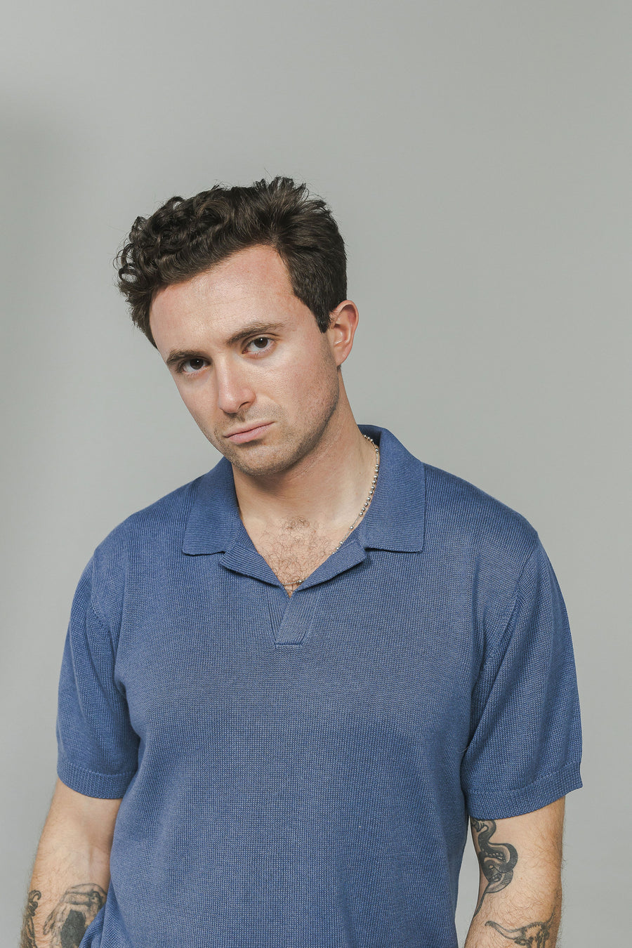 A portrait of a man in a slate blue knit polo shirt.