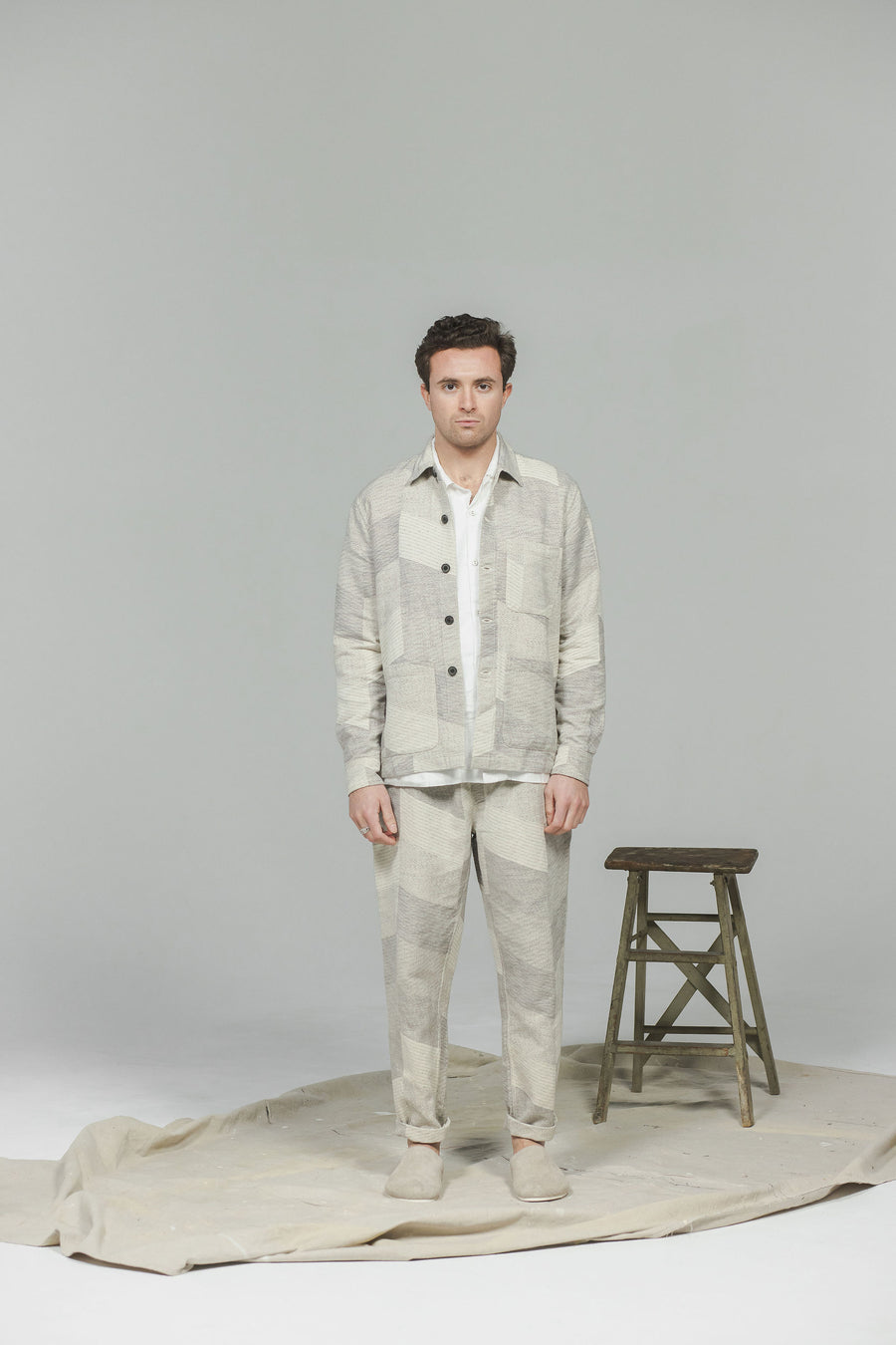 A man in a white and grey jacquard patterned suit and grey sandals.