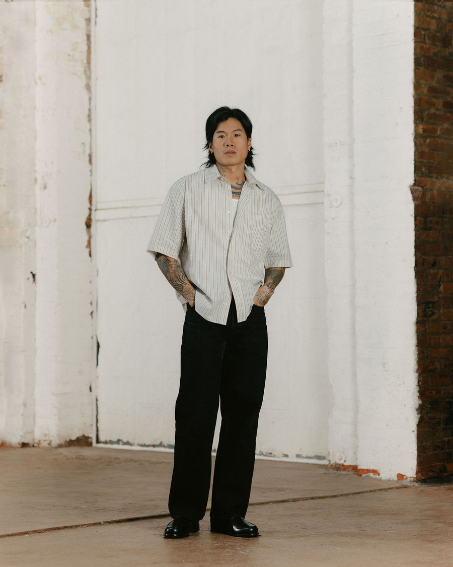 A man in a wide striped shirt and flowy black pants poses for the camera.