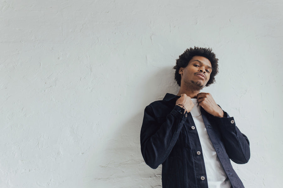Model grasps collar of jacket while leaning back against a wall