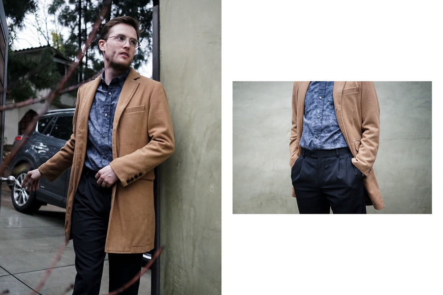 A man in a camel overcoat and 3sixteen BD shirt in charcoal haze walks briskly through a door.