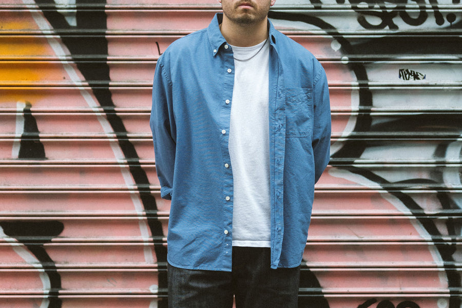 A man in a blue shirt over a white tshirt stands in front of a steel gate.