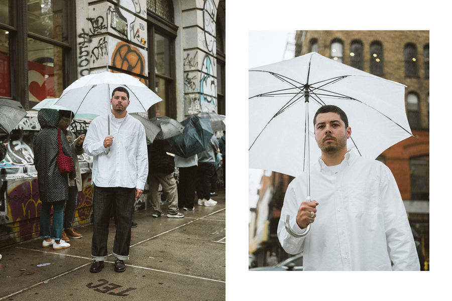 A man in a white oxford and white umbrella stands among a sea of other umbrellas.