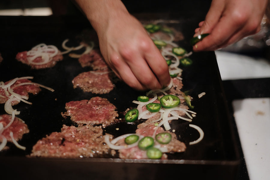 Smashburgers with jalapenos and onions on the griddle.