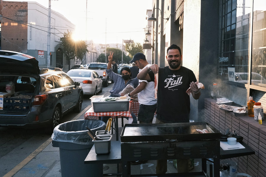 Three people setting up griddles outside on the sidewalk.