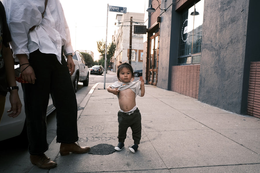 A little kid pulls his tshirt up on the sidewalk.