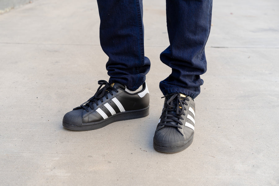 Tapered jeans stack on top of black Adidas Superstar sneakers.