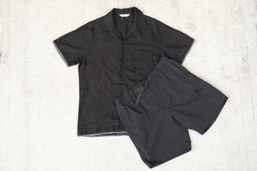 A black linen shirt and nylon shorts on a concrete floor.