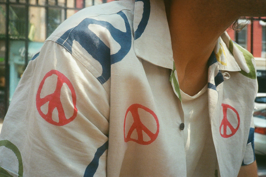A close up shot of the multicolored peace shirt. It has a tan colored body and the peace signs vary in color and size.
