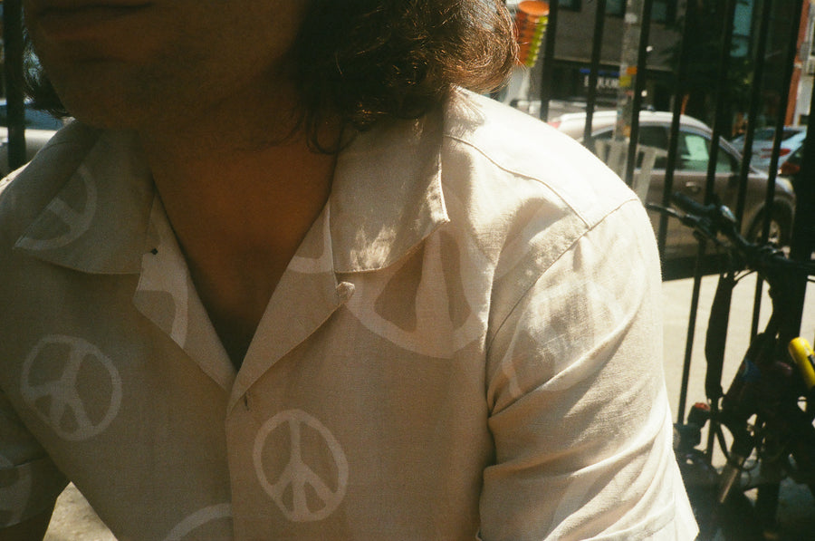 A moody yellow-tinged film image of a man wearing a white shirt with peace signs printed all over.