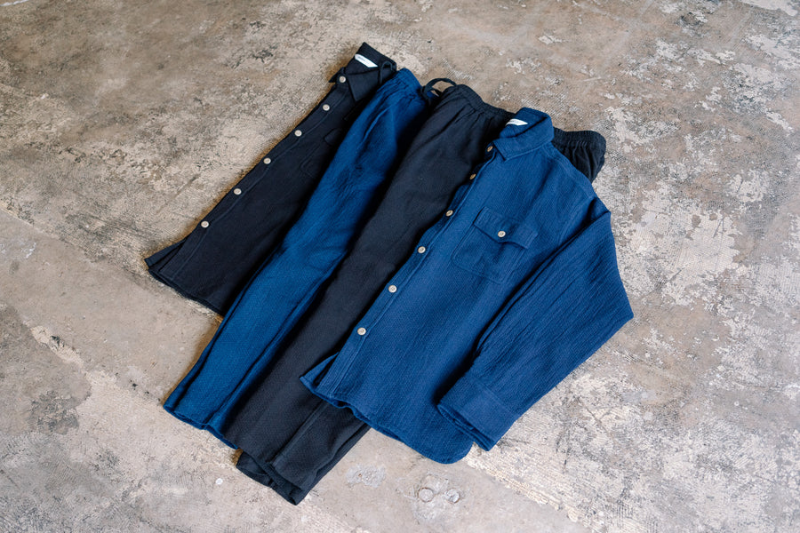 Two shirts and two pants in blue and black lie on a concrete floor.
