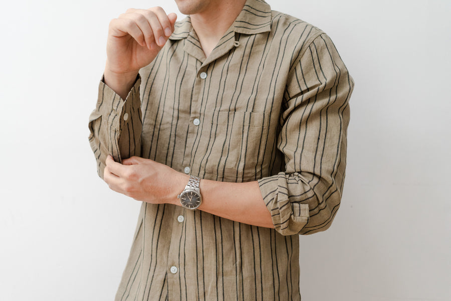 A close up shot of a man in a striped olive shirt adjusting his sleeve placket.
