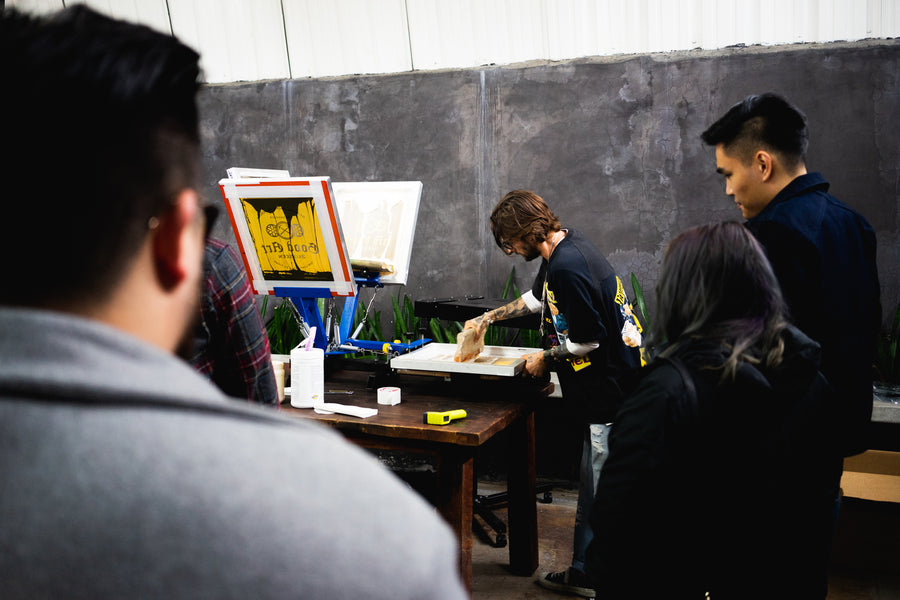 A crowd gathers around the silk screen printer as he prints onto garments at the event.