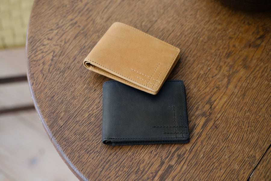 Two bifold wallets in black and tan sit on a table.